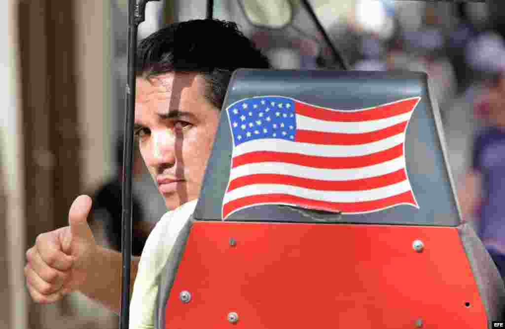 Un hombre saluda desde una bicitaxi con la bandera de EEUU.