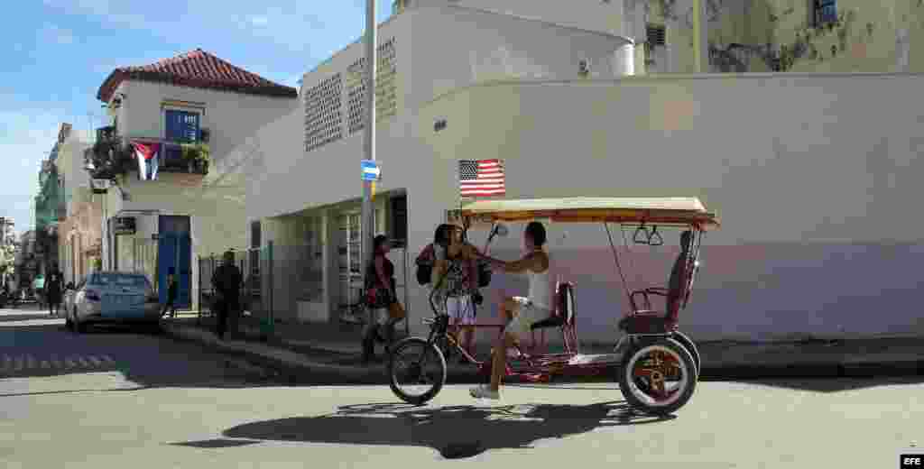 Un hombre pedalea en su bicitaxi con la bandera de Estados Unidos.