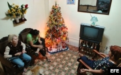 Tres mujeres conversan en una casa decorada con un árbol de Navidad.